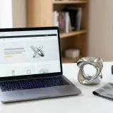 清潔な白いデスクに置かれたノートパソコンと、丁寧に磨かれた金属のオブジェ。質を高めること（ブラッシュアップ）を表現している。明るい自然光のプロフェッショナルな写真。