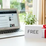 清潔な白いデスクに置かれたノートパソコン。その横には「FREE」と書かれたカードと、赤いリボンがかかった小さなギフトボックスが置かれている。