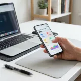 清潔な白いデスクに置かれたノートパソコンと、最新のスマートフォン。スマートフォンを操作する手が映り、直感的で心地よい操作体験（UX）を表現している。