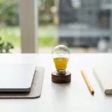 清潔な白いデスクに置かれたノートパソコン。その横には、一本の鉛筆と、まだ明かりがついていない小さな色鮮やかな電球が置かれ、閃き（ジャストアイデア）を表現している。