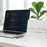 清潔な白いデスクに置かれたノートパソコン。その横には、0から10までの目盛りが描かれたカードと小さなハートの置物があり、顧客の愛着度（NPS）を表現している。明るい自然光のプロフェッショナルな写真。