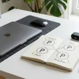 清潔な白いデスクに置かれたノートパソコン。その横には、4つのP（Product, Price, Place, Promotion）が書かれた図解と製品サンプルがあり、マーケティング戦略（4P分析）を表現している。