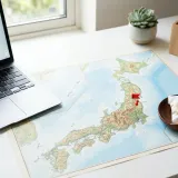 清潔な白いデスクに置かれたノートパソコン。その横には、日本地図があり、地方の都市にピンが立てられている。国内の地方拠点との連携（ニアショア）を表現している。